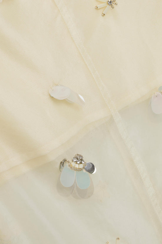Cream organza fabric with scattered crystal and pearl embellishments, including teardrop-shaped beads and dangling charm deta