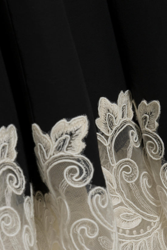 Black midi dress with cream lace hem featuring ornate scrollwork and leaf motifs.