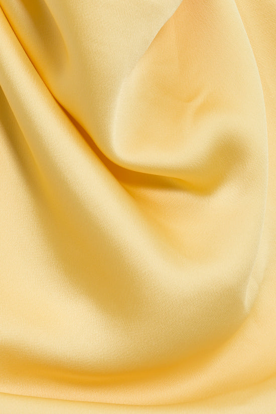 Light yellow satin fabric with draped folds and soft shadows.