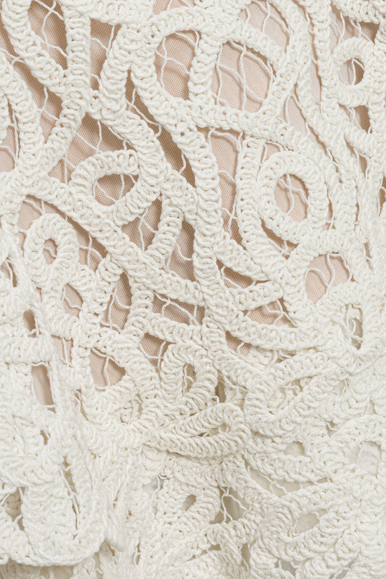Cream lace fabric with ornate scrolling pattern and cutout details on neutral background.