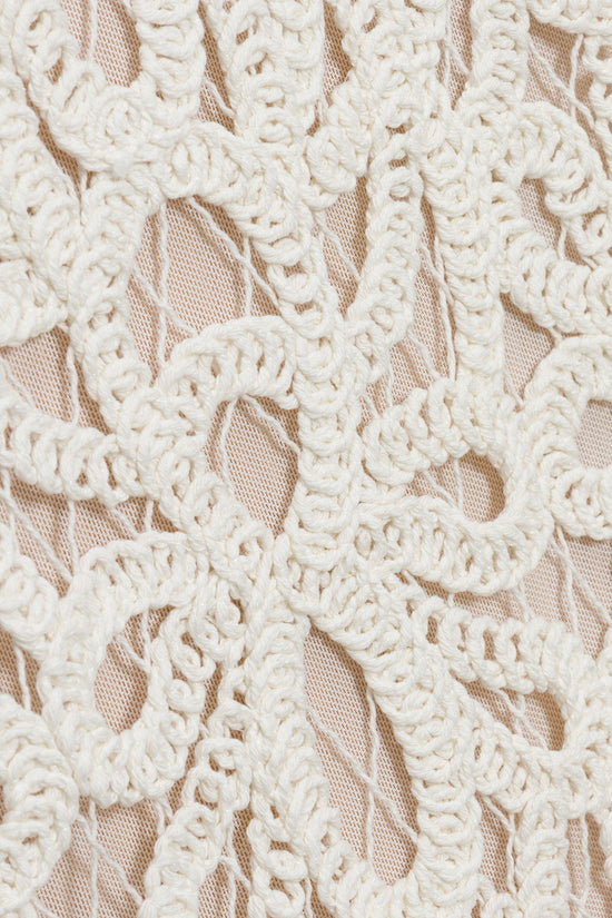 White lace with ornate scrollwork pattern over nude underlay fabric.