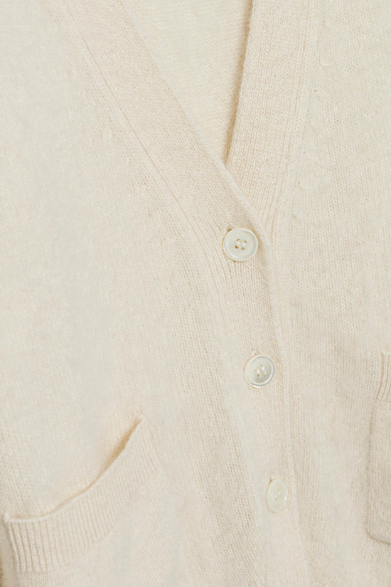Cream brushed knit cardigan with white buttons and ribbed trim visible on front placket and pocket.