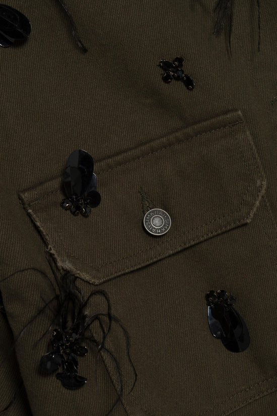 Olive-green denim jacket with black beaded embellishments and metal button details scattered across the surface.