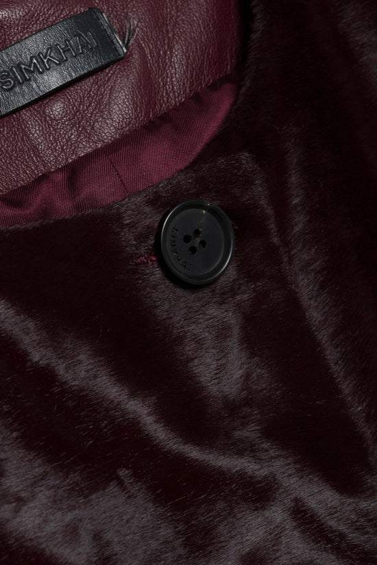 Black calf hair coat with dark button closure, burgundy interior lining, and brand label visible.