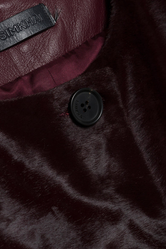 Black calf hair coat with dark button closure, burgundy interior lining, and brand label visible.