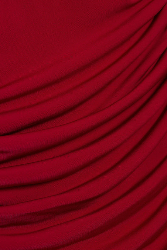 Red draped jersey fabric with flowing folds and diagonal texture detail.