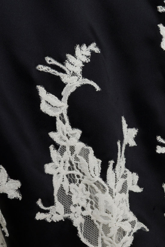 Black fabric with white lace floral embroidery featuring flowering botanical motifs.