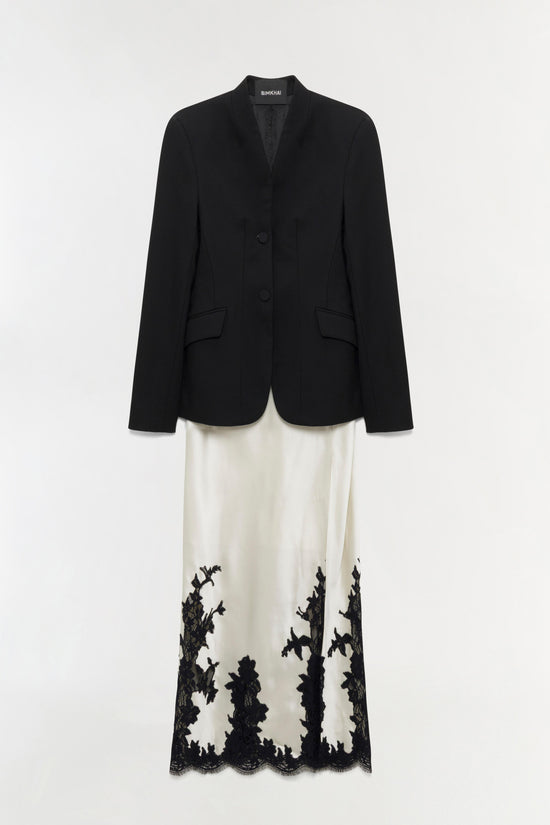 Black blazer layered over cream maxi dress with black lace hem detail.