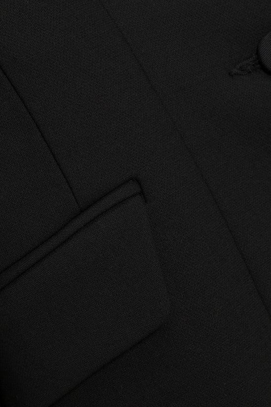 Black textured fabric with structured blazer seams and folds visible throughout.