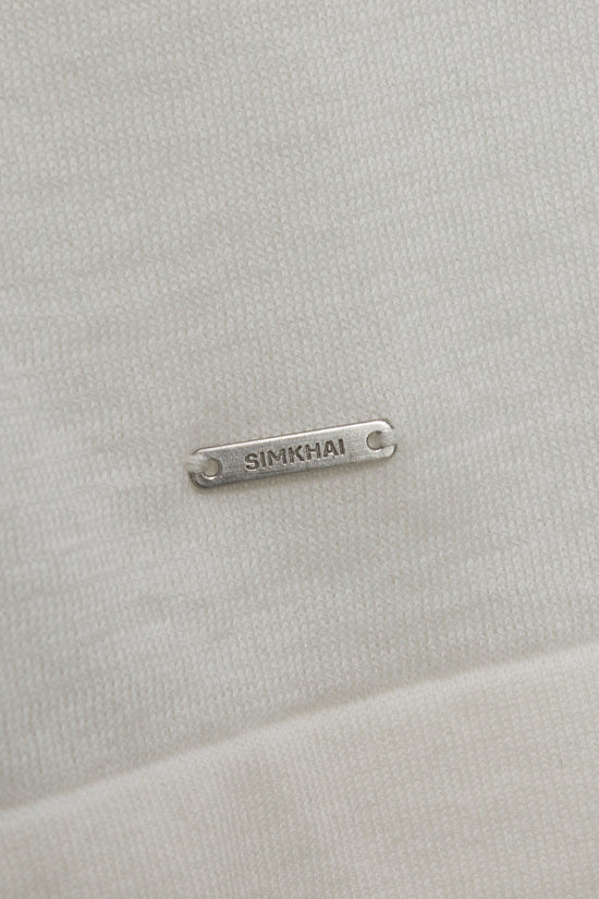 Silver metal nameplate with "SIMKHAI" engraved text on beige textured fabric surface.