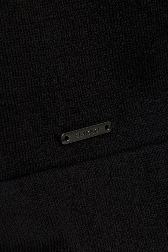 Black ribbed polo shirt with metal brand nameplate detail on chest.