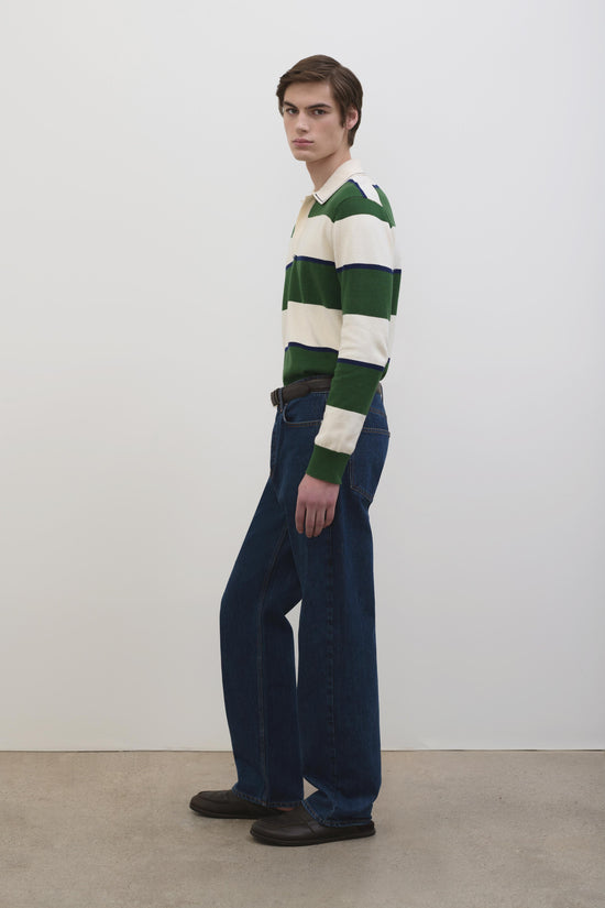 Man wearing green, cream, and navy striped popover with dark denim jeans and brown shoes.