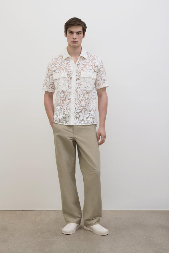 White and beige lace short-sleeve shirt with collar and front chest pockets worn with khaki pants.
