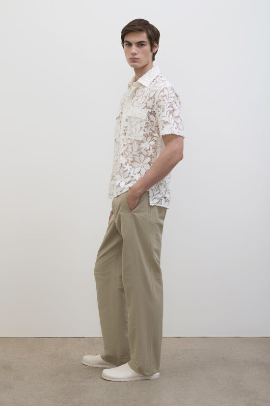 Man wearing white lace short-sleeve shirt with collar and beige trousers, styled with white shoes.