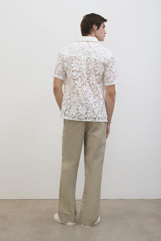 White floral lace short-sleeve shirt with collar, worn with beige trousers.