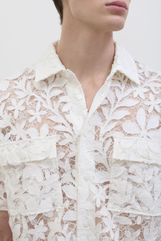 White cotton lace button-up shirt with leafy pattern and white collar, worn by model shown from neck down.