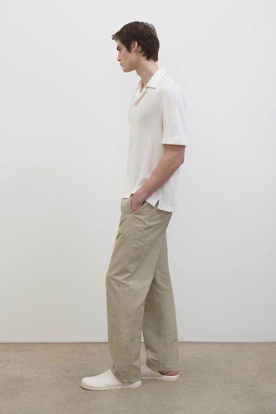 Man wearing cream waffle-textured short-sleeve button-up shirt with beige pants and white slip-on shoes.