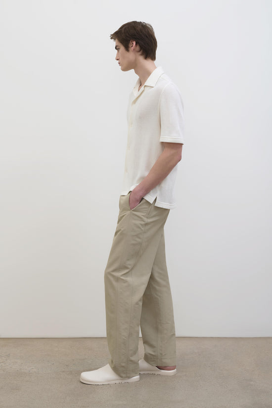 Man wearing cream waffle-textured short-sleeve button-up shirt with beige pants and white slip-on shoes.