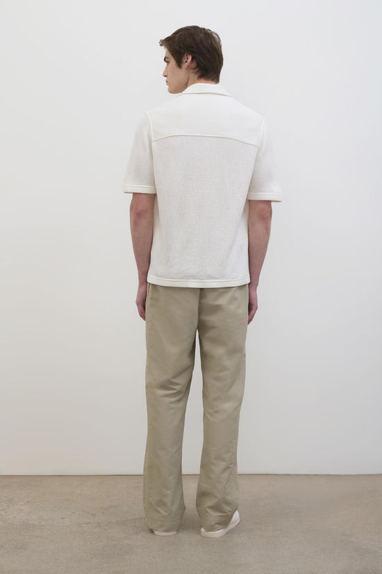 Man wearing cream waffle-textured short-sleeve collared shirt with beige pants, shown from behind.