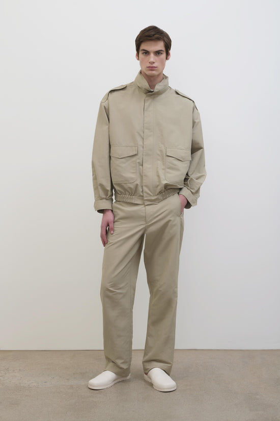 Man wearing beige technical jacket with chest pockets and matching trousers paired with white slip-on shoes.