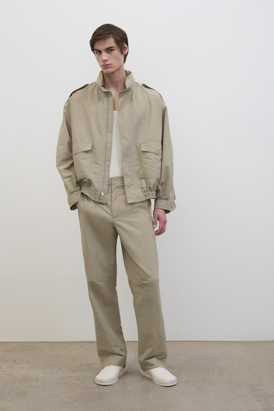 Man wearing beige Shane Tech Jacket with chest pockets, paired with matching pants and white shirt underneath.