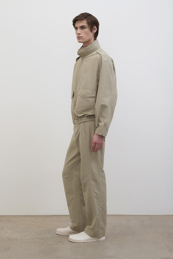 Beige tech jacket with high collar and cargo pockets styled with matching pants and white slides.