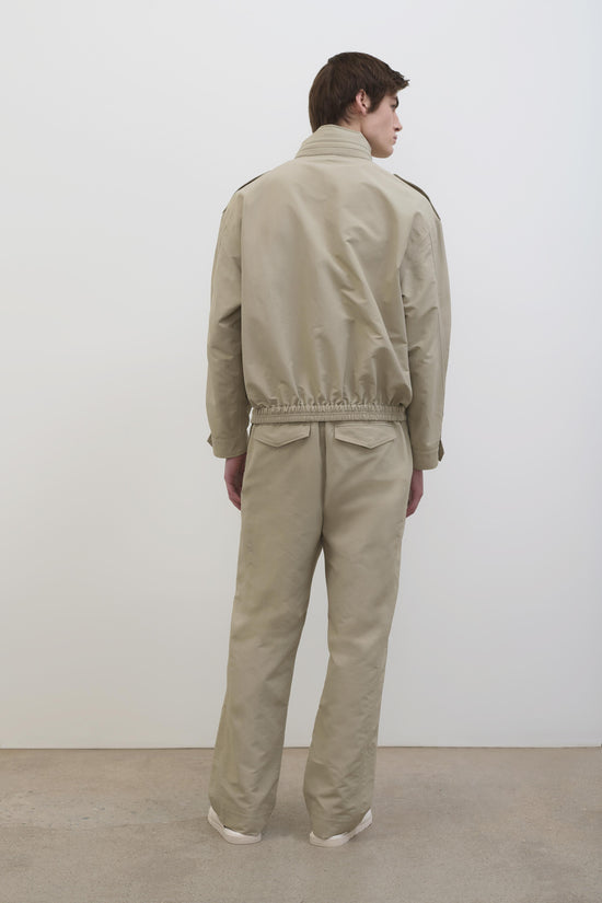 Beige tech jacket with high collar and elasticated waist, shown from back on model wearing matching pants.
