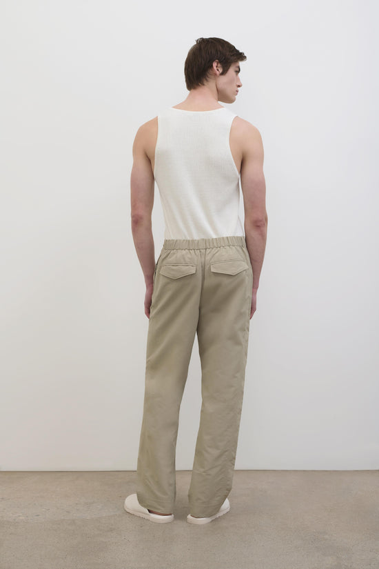 Beige tech pant with elastic waistband and flap pockets, shown from back on model wearing white tank top.