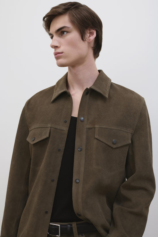 Olive-brown suede utility jacket with button front, chest pockets, and pointed collar worn by model.