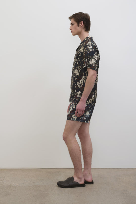 Black silk shirt with cream floral print, short sleeves, worn by model in side profile view.