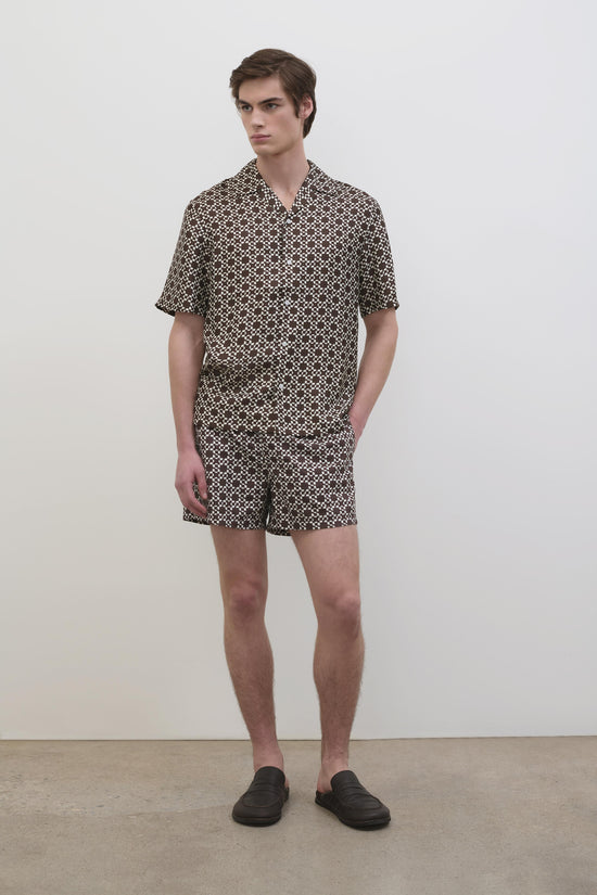 Man wearing Malachi swim shorts with small-scale geometric pattern in brown and cream, paired with matching short-sleeve shir
