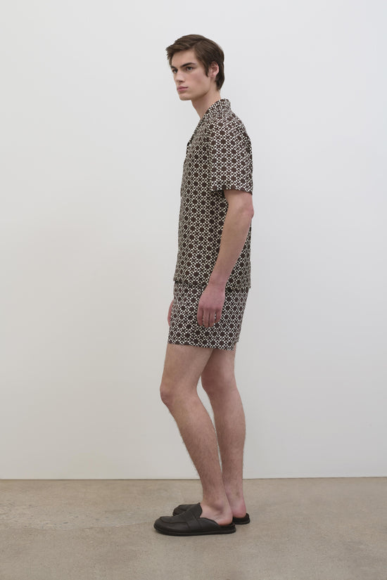 Man wearing short-sleeved shirt dress with brown and cream geometric print pattern.