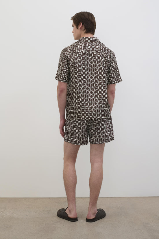 Man wearing brown and white geometric printed silk shirt with matching shorts, shown from back view.