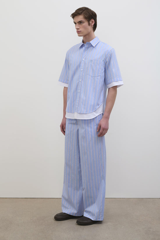 Light blue striped short-sleeve cotton shirt with white button front and chest pocket, worn with matching striped pants.