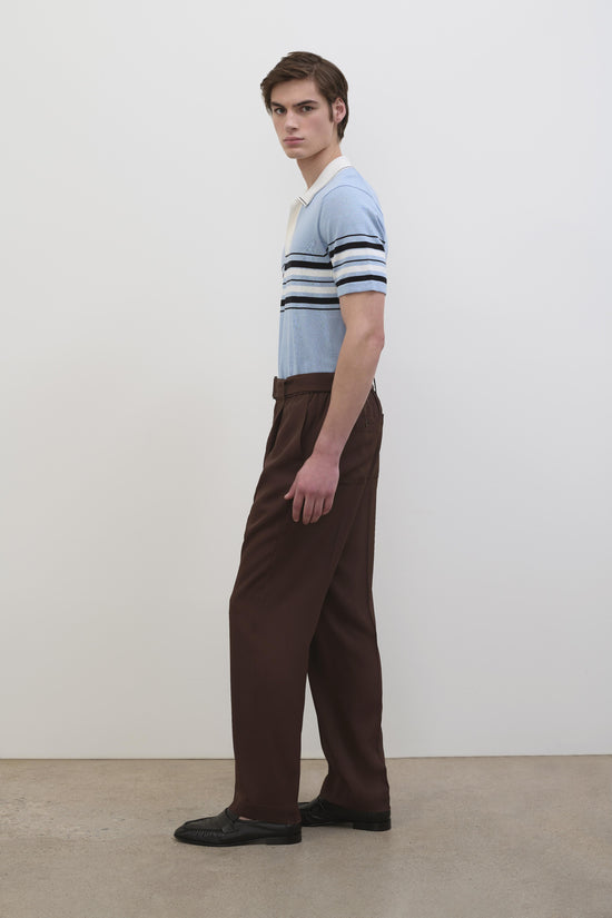 Men's light blue cotton knit popover with dark and white striped sleeves, paired with brown trousers.