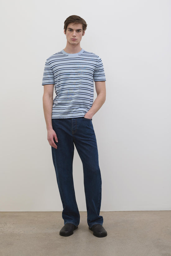 Man wearing light blue striped short-sleeve t-shirt with dark blue horizontal stripes and dark denim jeans.