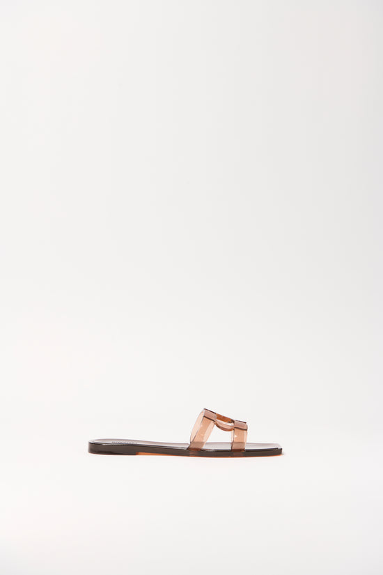 Transparent peachy jelly flat slide with monogram bow detail and dark sole, shown in profile view.