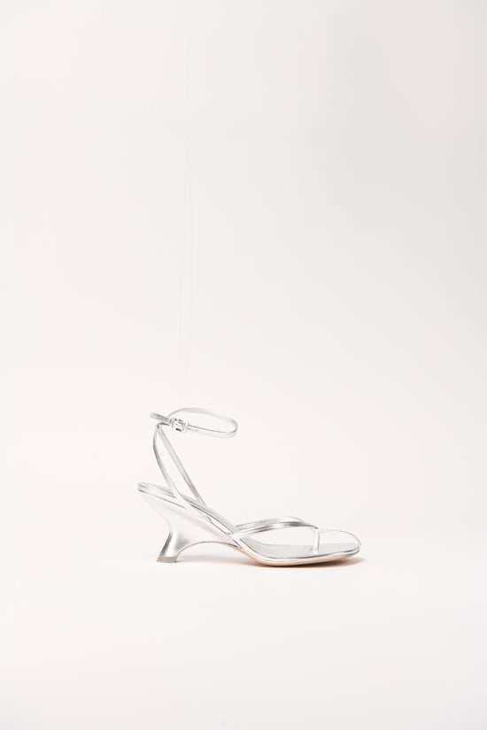 Silver metallic leather strappy wedge sandal with ankle buckle strap and curved wedge heel.