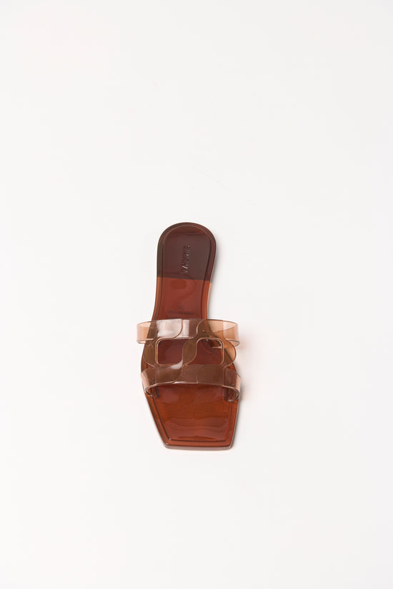 Translucent brown jelly flat slide with monogram straps across the foot, viewed from above on neutral background.