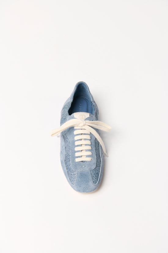 Blue denim sneaker with cream laces and leather accents, viewed from above.