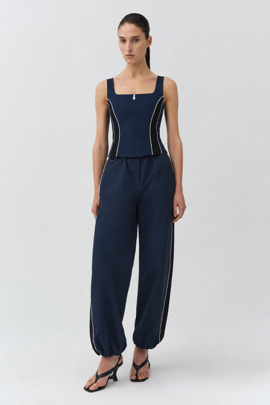 Woman wearing navy sleeveless bustier top with white piping and matching cropped tapered pants.