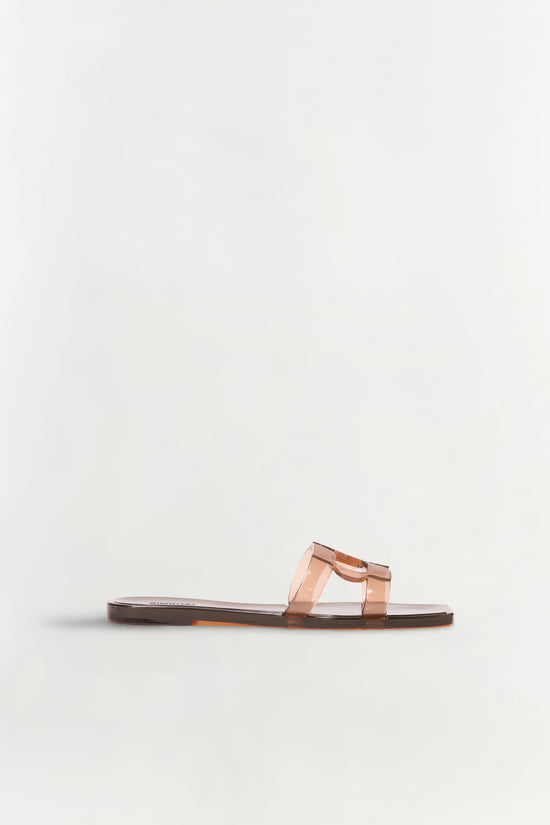 Transparent peach-colored jelly flat slide with monogram strap detail and dark brown sole.