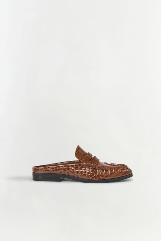 Brown leather loafer mule with crocodile texture, black sole, and buckle detail on upper.