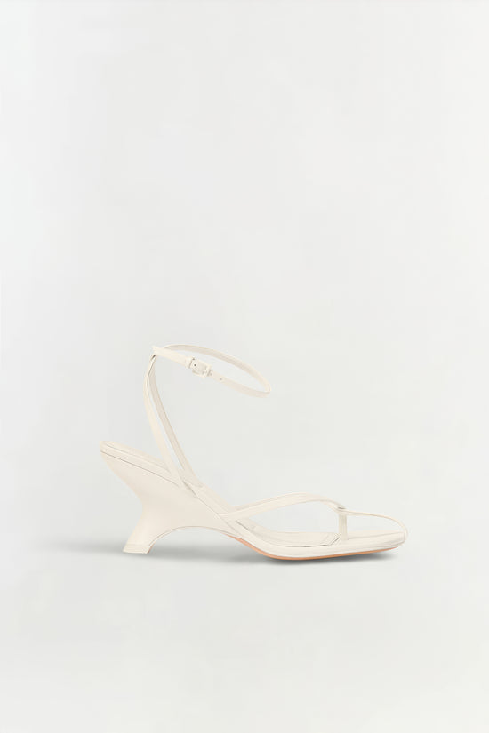 Cream leather strappy wedge sandal with ankle buckle strap and curved wedge heel.