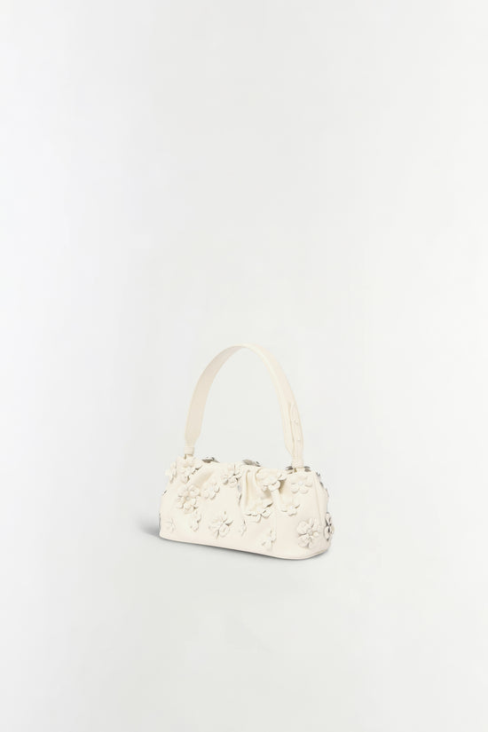 Cream leather shoulder bag with dimensional floral appliqués across the front and single handle.