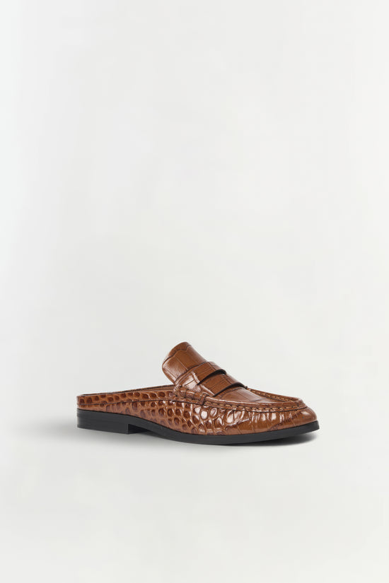 Brown crocodile-textured leather loafer mule with black sole, shown from the side view.