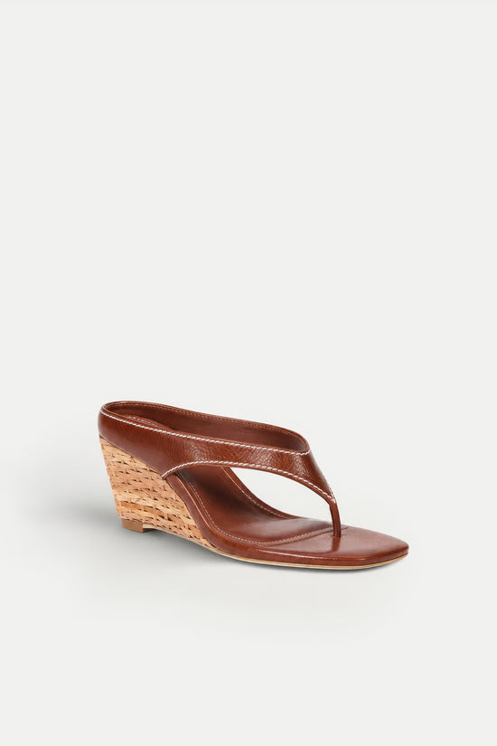 Brown leather thong sandal with woven wedge heel and open toe design.