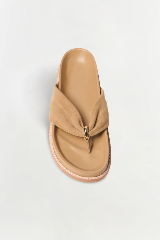 Beige suede thong sandal with a folded toe strap and metal ring detail, viewed from above.