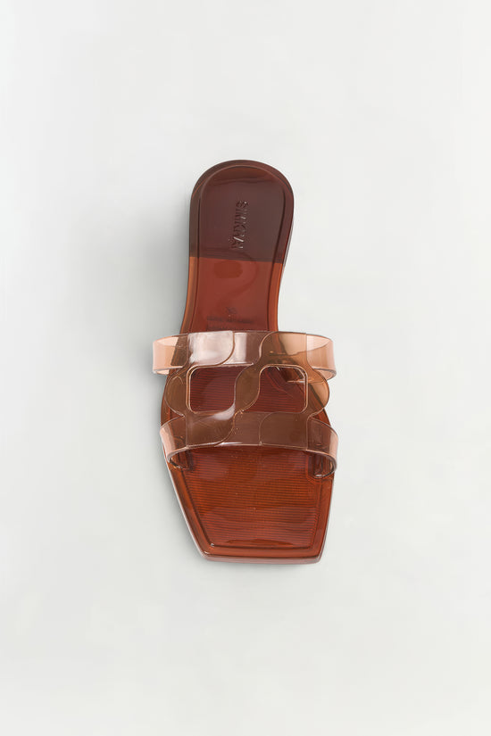 Clear jelly slide sandal with monogram cutout detail in coral and brown tones, shown from above.